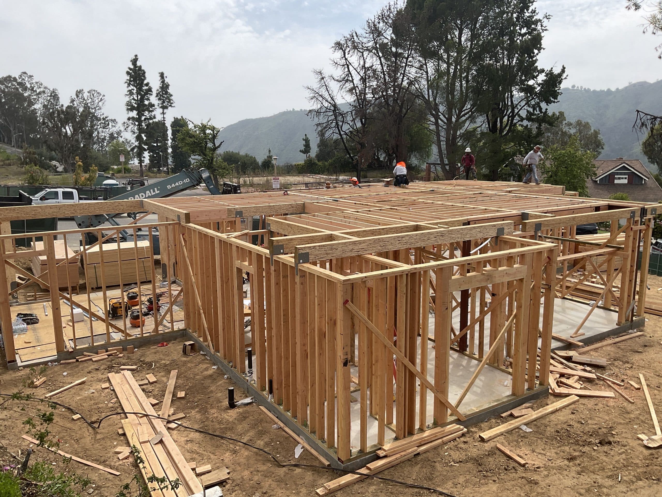 Two-story wood framing of the fire-resistant rebuild rising against the Santa Monica Mountains
