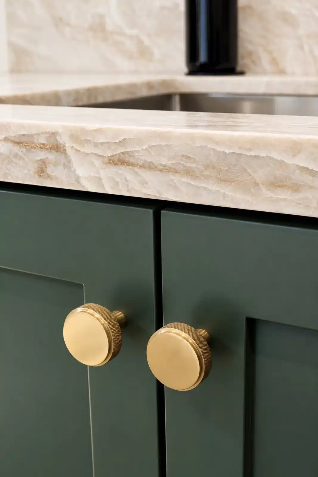 Green shaker cabinet doors with brass knobs under quartzite