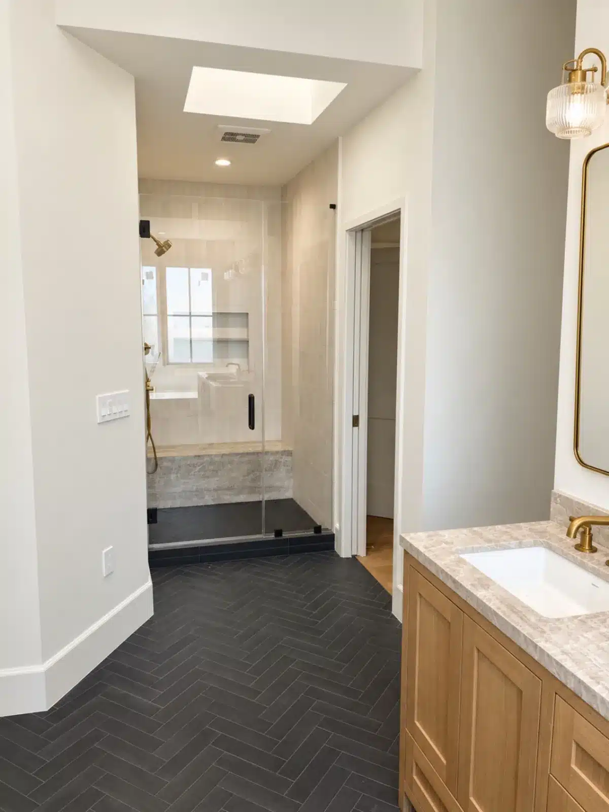 Primary bathroom with black herringbone floor and skylight over the shower