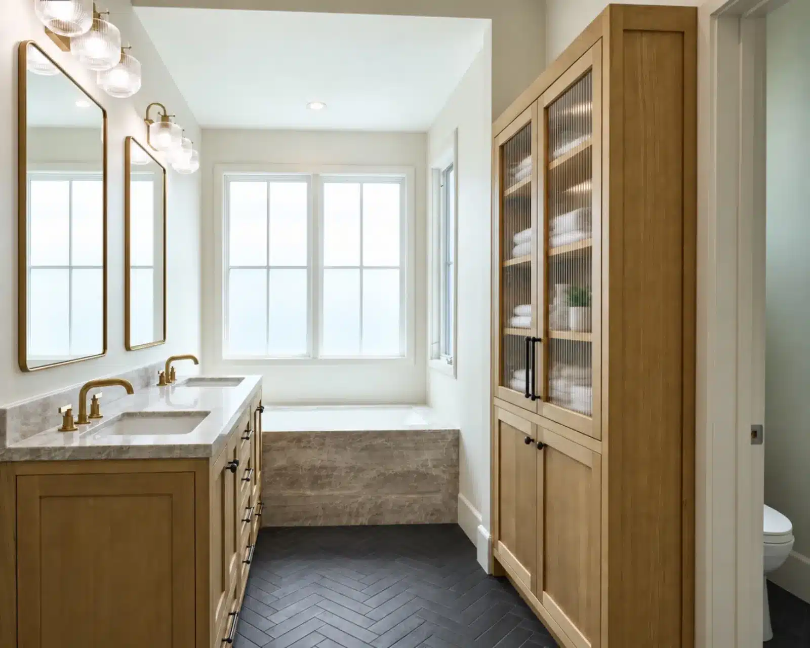 Primary bathroom with oak double vanity, linen cabinet and soaking tub