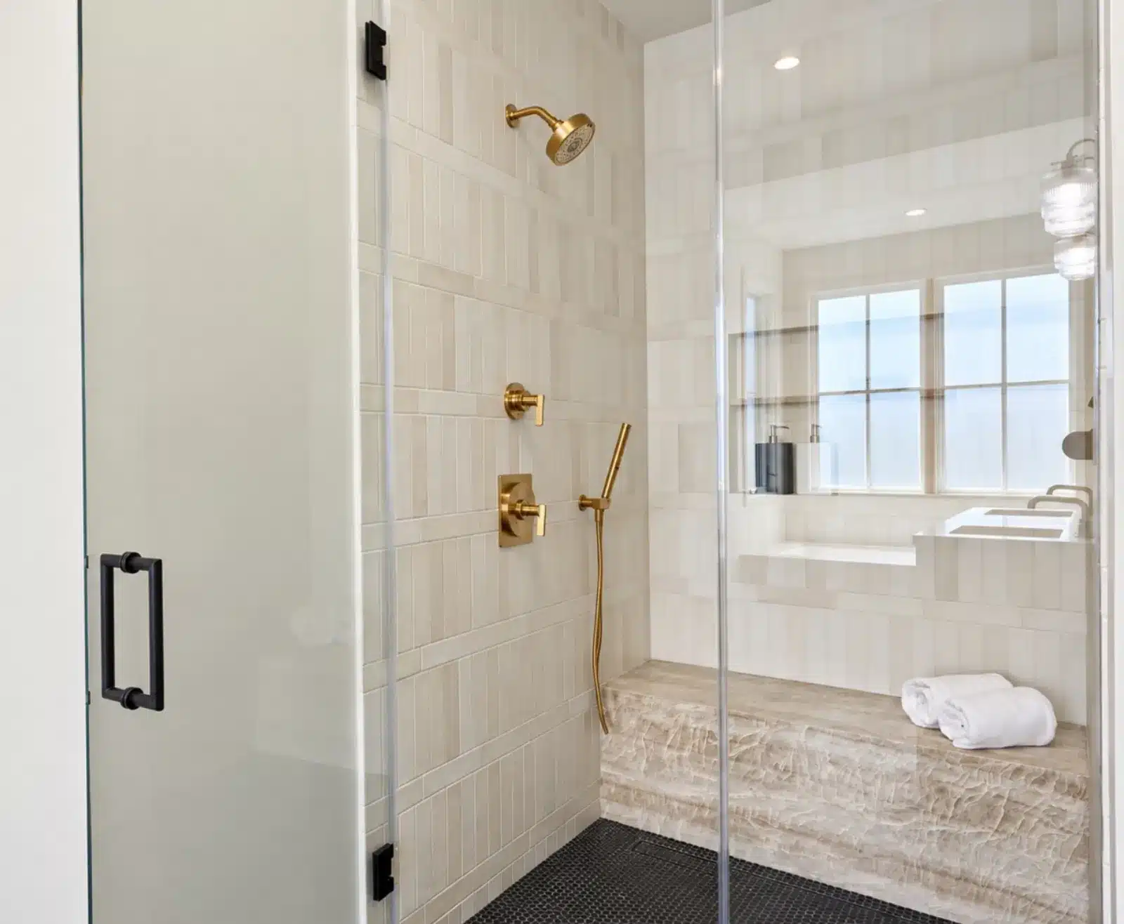 Walk-in primary shower with glass enclosure, quartzite bench and brass fixtures
