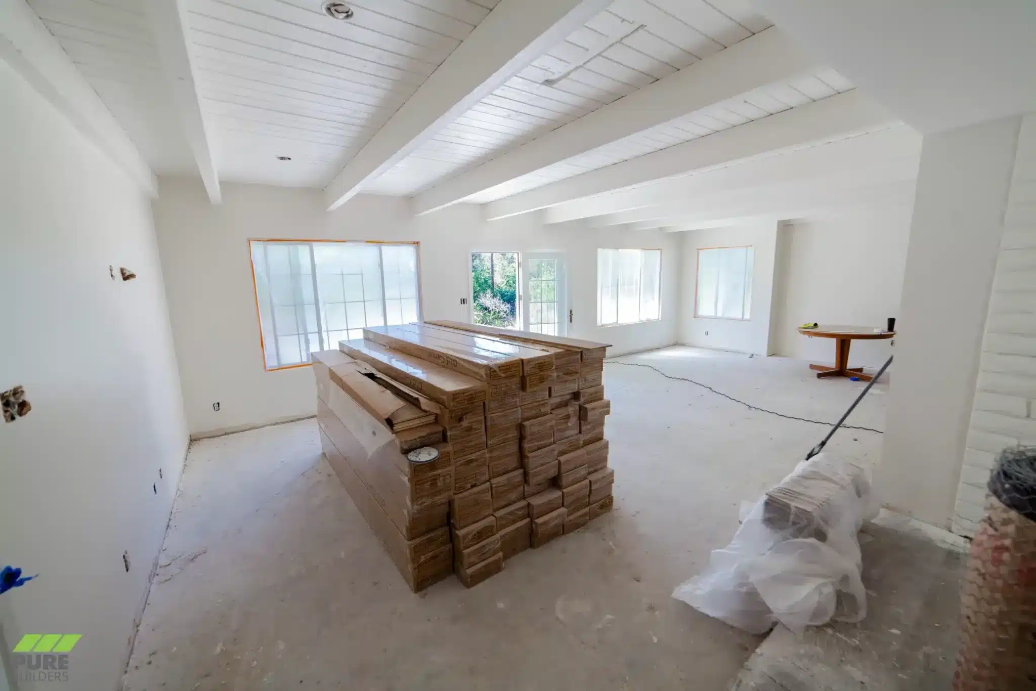 Unfinished room with white ceiling beams, exposed outlet boxes, and stacked flooring boxes on a bare floor.