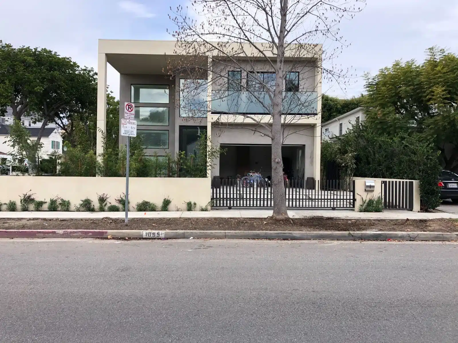Modern white house with large windows, black fence, and bare tree in front yard.