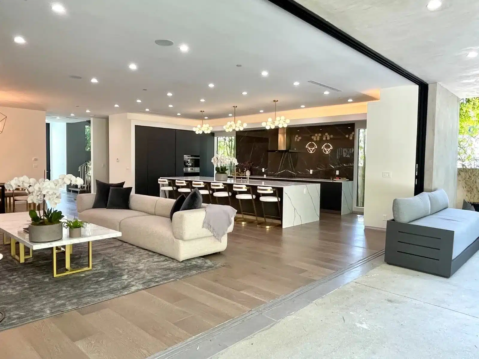 Modern living room and kitchen with curved cream sofa, black and white island, dark cabinetry, and pendant lights